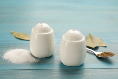 White ceramic salt and pepper shakers, bay leaves with spoon on turquoise wooden table, closeup