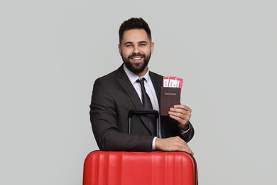 Photo of Happy businessman with passport, tickets and suitcase on grey background
