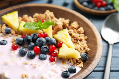 Image of Tasty granola with yogurt, berries and sliced pineapple for breakfast on blue wooden table, closeup