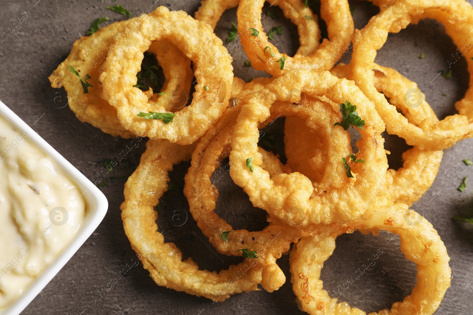 Photo of Homemade crunchy fried onion rings with sauce on color table, top view