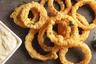 Photo of Homemade crunchy fried onion rings with sauce on color table, top view