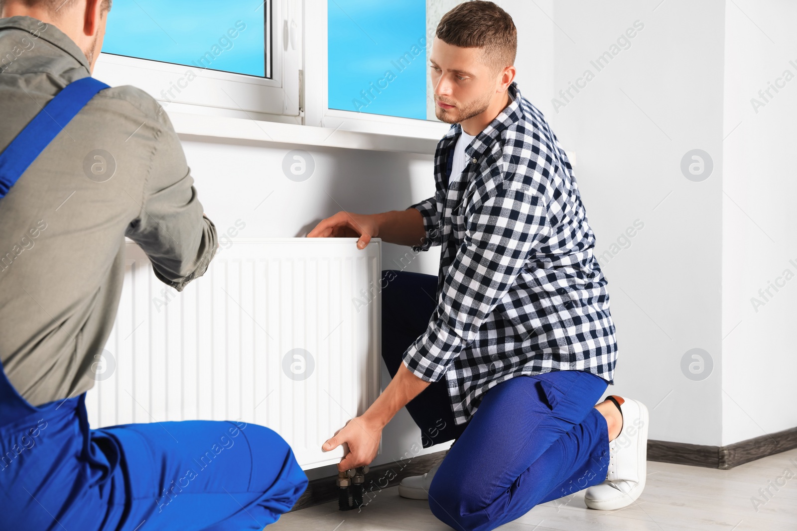 Photo of Professional plumbers installing new heating radiator in room