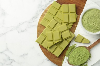 Pieces of tasty matcha chocolate bar and powder on white marble table, top view. Space for text