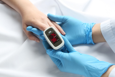 Photo of Doctor examining patient with fingertip pulse oximeter in bed, closeup