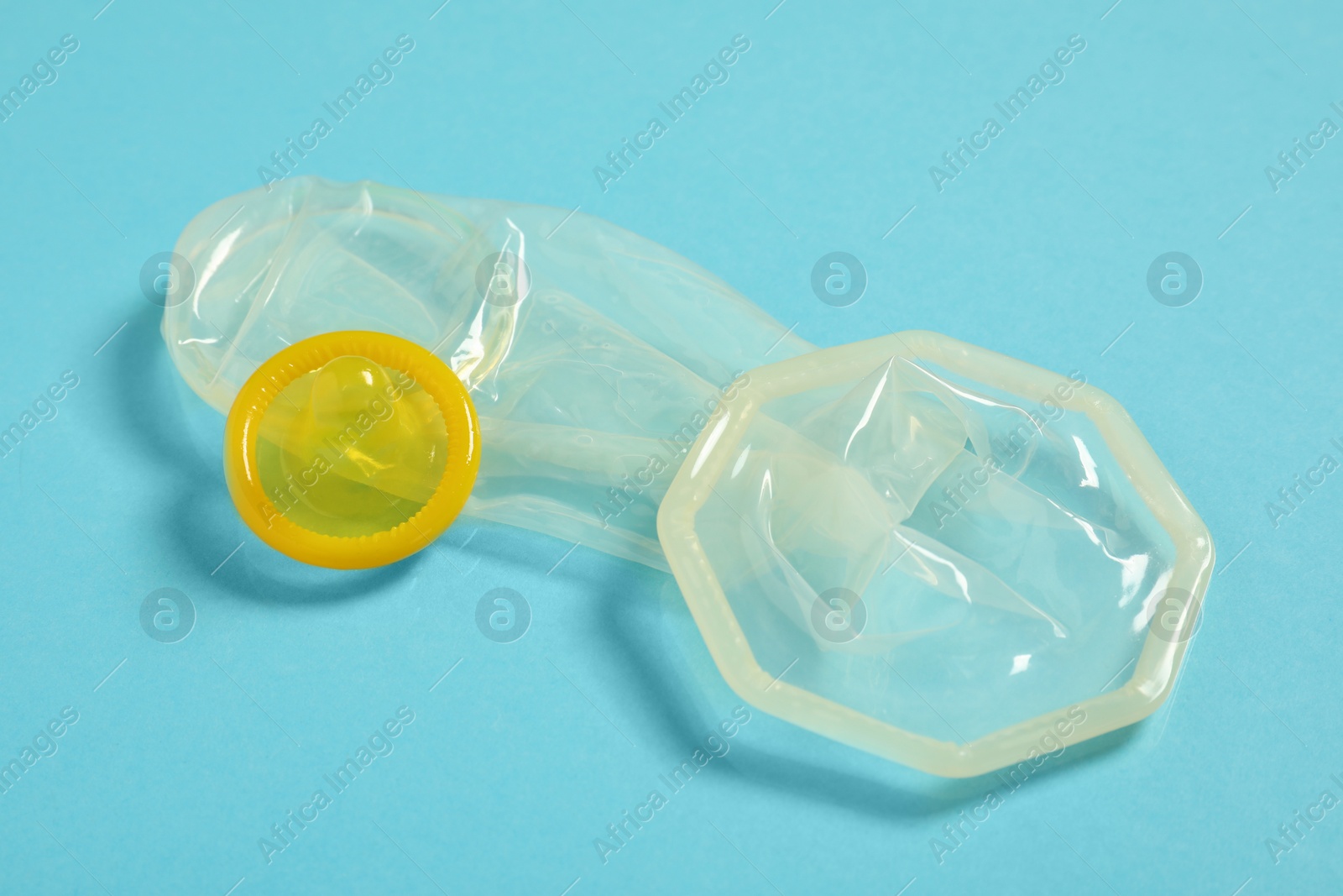 Photo of Unrolled female and male condoms on light blue background, closeup. Safe sex