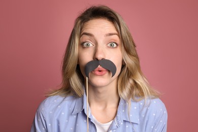 Emotional woman with fake mustache on dusty rose background