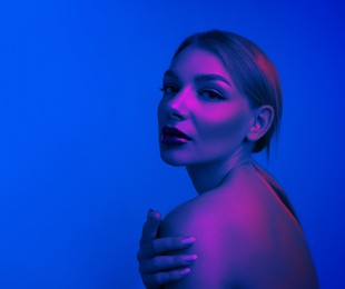 Image of Young woman with beautiful makeup posing in neon lights against blue background