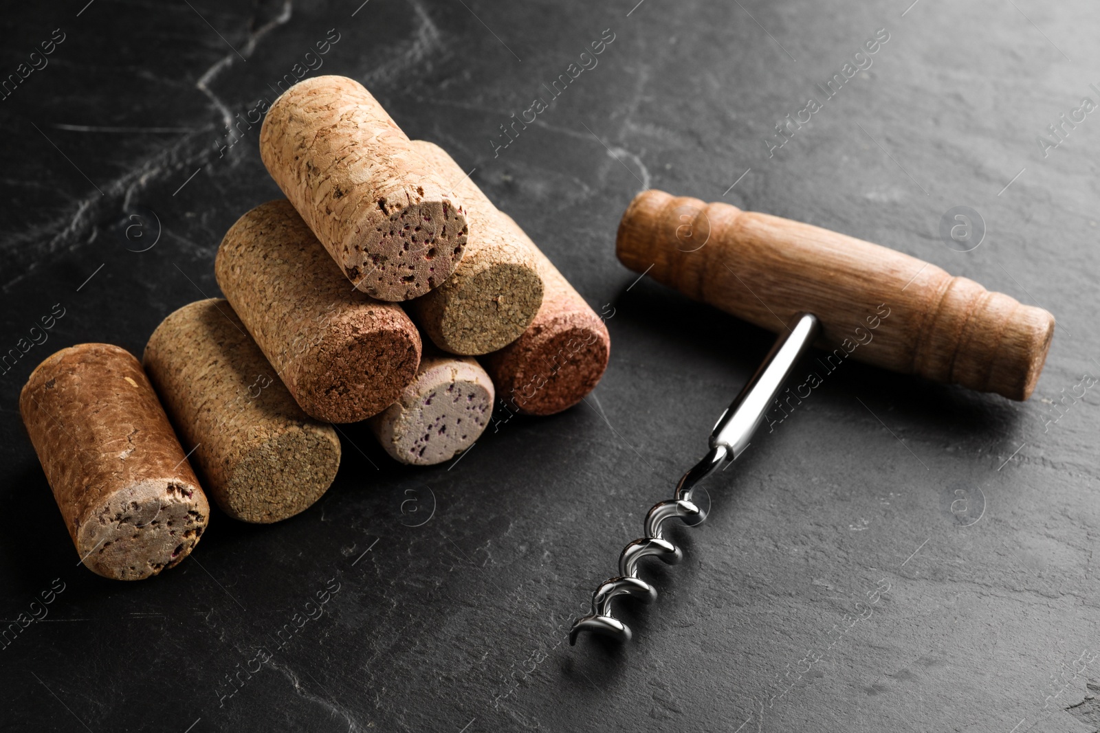 Photo of Corkscrew and stack of wine bottle stoppers on slate table, closeup