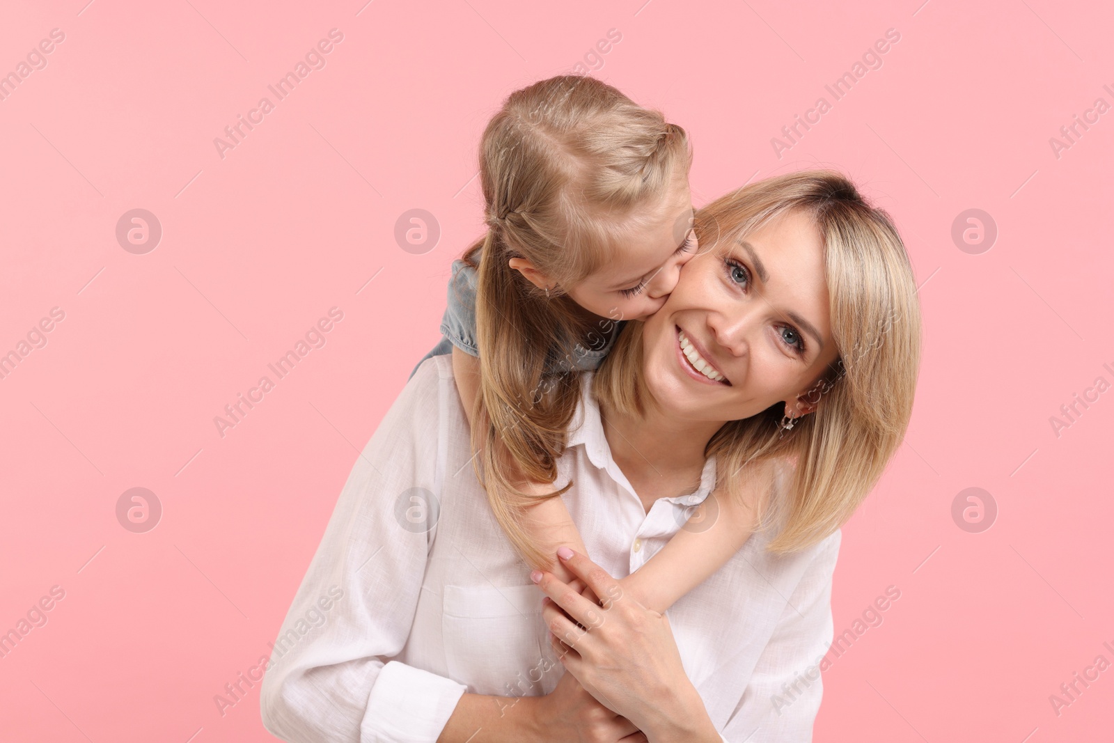 Photo of Daughter hugging and kissing her happy mother on pink background