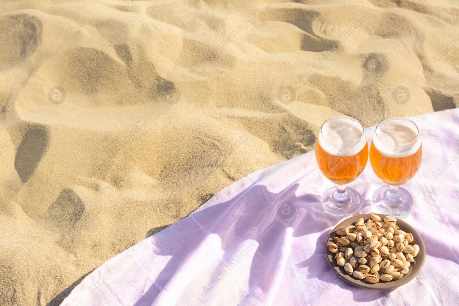 Photo of Glasses of cold beer and pistachios on sandy beach, above view. Space for text