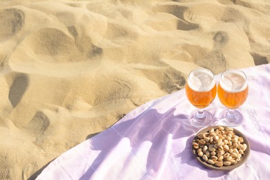 Photo of Glasses of cold beer and pistachios on sandy beach, above view. Space for text