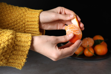 Photo of Woman peeling fresh ripe tangerine on black background, closeup