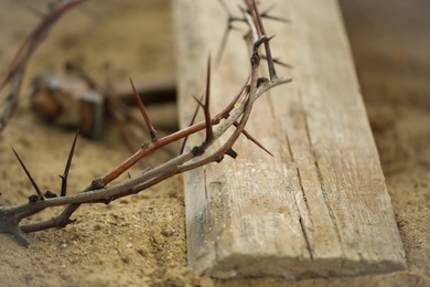 Crown of thorns and wooden plank on sand, closeup. Easter attribute