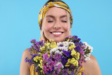 Photo of Portrait of smiling hippie woman with bouquet of flowers on light blue background