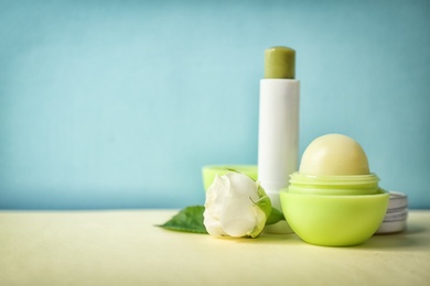 Photo of Hygienic lipstick and balm on table against color background