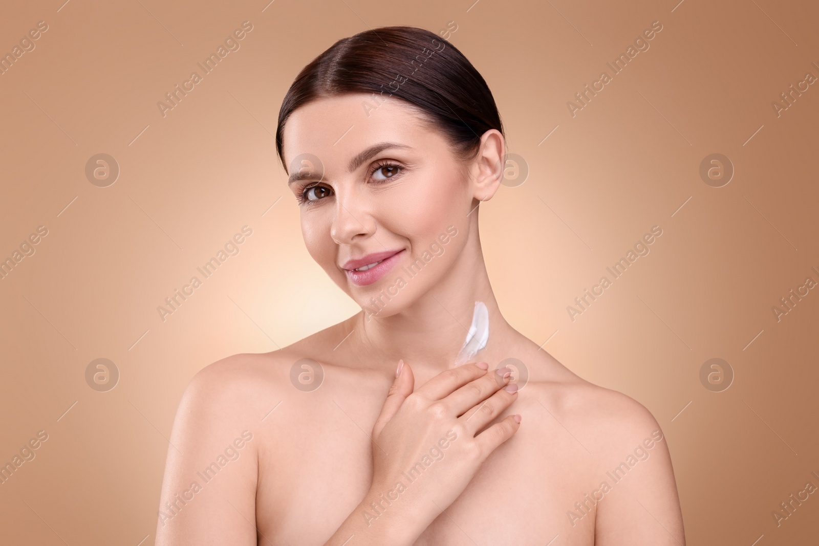Photo of Beautiful woman with smear of body cream on her neck against light brown background