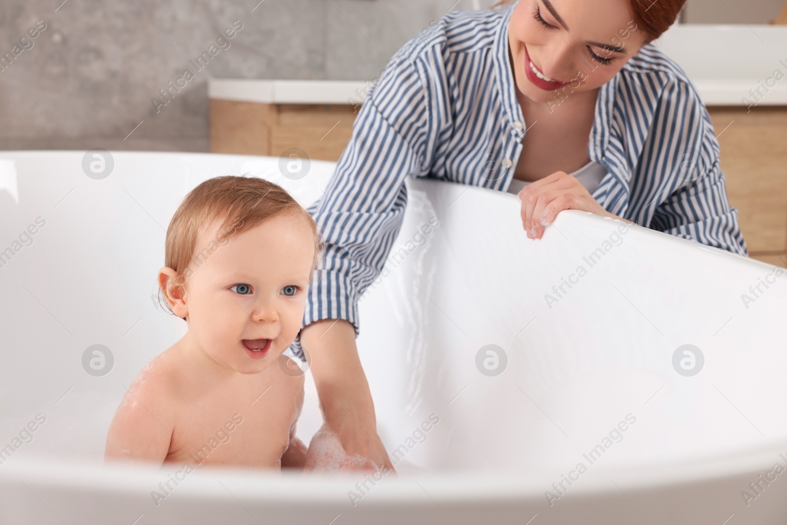 Photo of Mother washing her little baby in tub at home, closeup