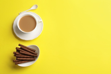 Photo of Delicious chocolate wafer rolls and cup of coffee on color background, top view with space for text. Sweet food