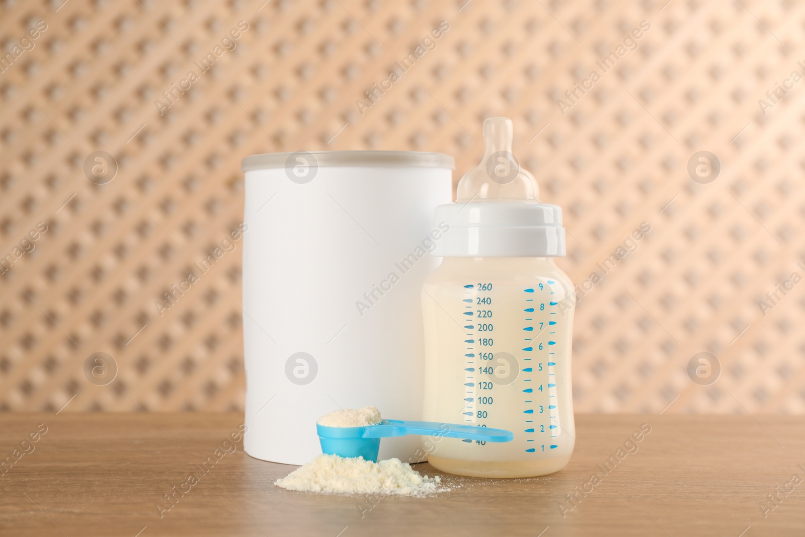 Photo of Blank can of powdered infant formula with feeding bottle and scoop on wooden table. Baby milk