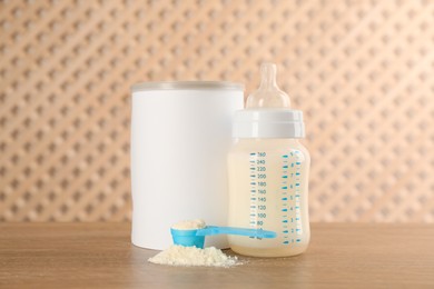 Photo of Blank can of powdered infant formula with feeding bottle and scoop on wooden table. Baby milk