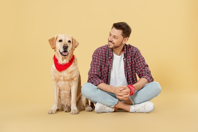 Happy man with his cute Labrador Retriever on beige background