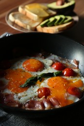 Photo of Fried with eggs, bacon and tomatoes in frying pan served with toasts on wooden table, closeup. Tasty breakfast