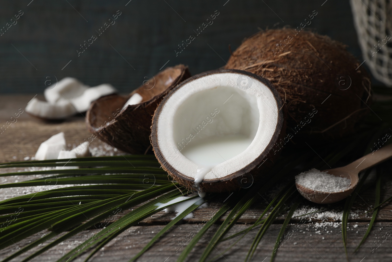 Photo of Coconut milk, flakes, nuts and palm leaf on wooden table, closeup