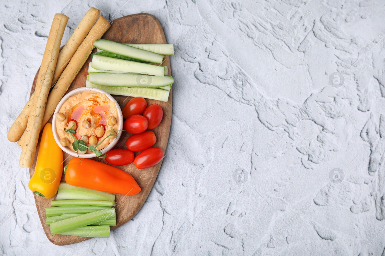 Photo of Board with delicious hummus, grissini sticks and fresh vegetables on light grey textured table, top view. Space for text