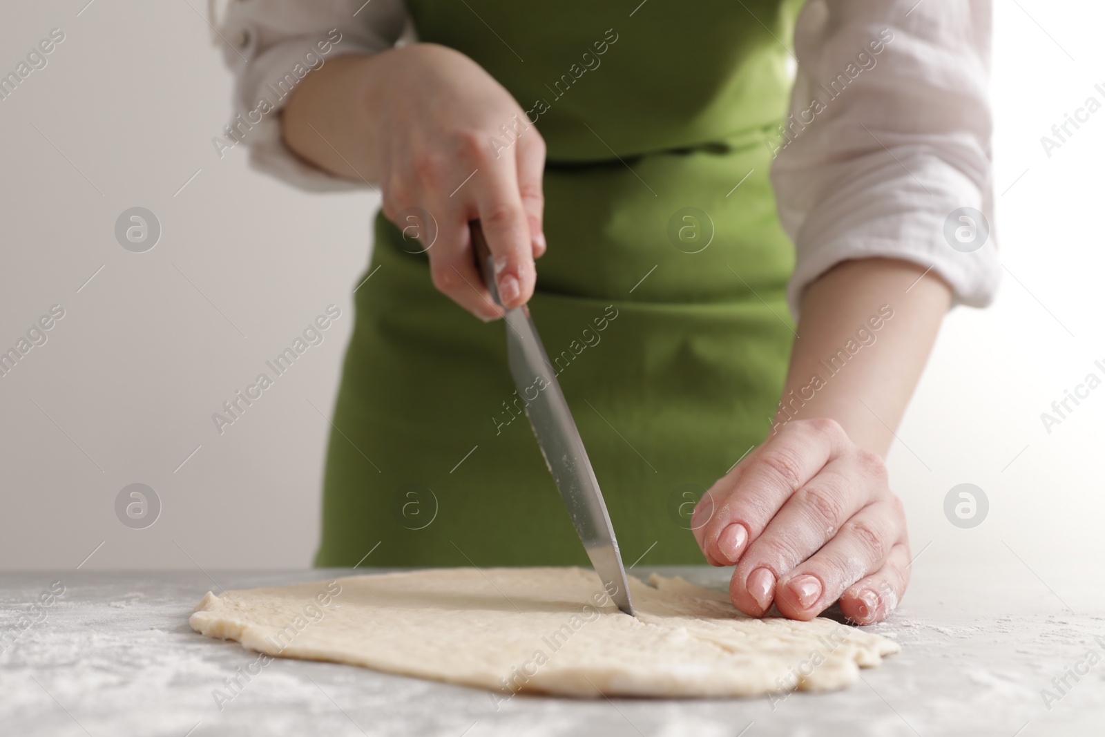 Photo of Woman cutting dough at light grey marble table, closeup. Cooking grissini