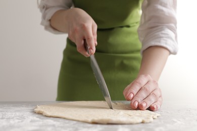 Woman cutting dough at light grey marble table, closeup. Cooking grissini