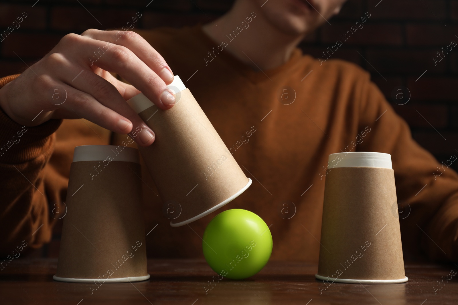 Photo of Shell game. Man showing ball under cup at wooden table, closeup