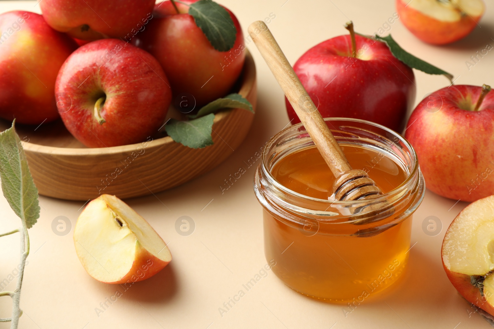 Photo of Delicious apples, jar of honey, leaves and dipper on beige background, closeup