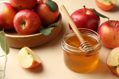 Delicious apples, jar of honey, leaves and dipper on beige background, closeup