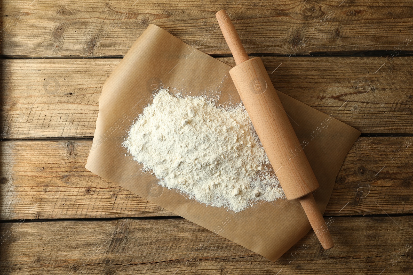 Photo of Parchment with flour and rolling pin on wooden table, top view