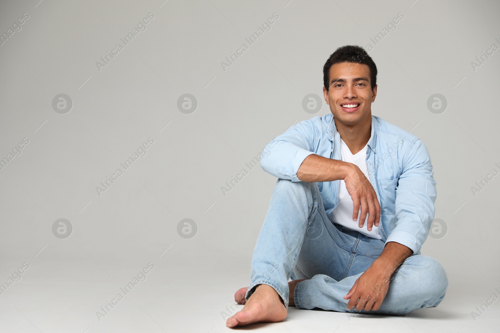 Photo of Handsome young African-American man sitting on light background. Space for text