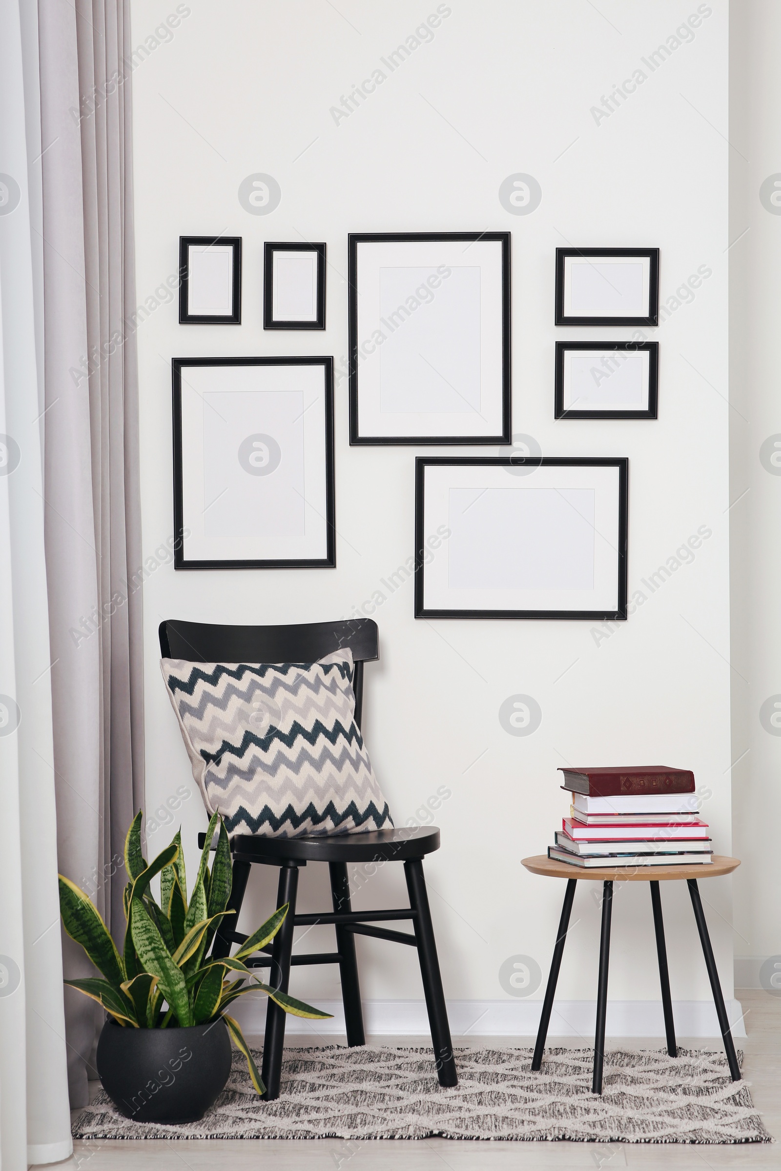 Photo of Empty frames hanging on white wall, wooden chair and table with books indoors