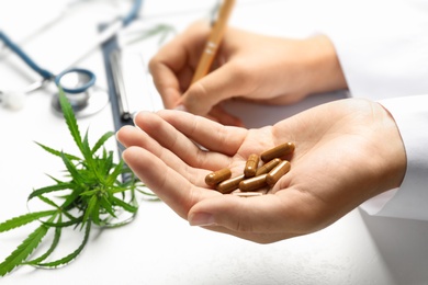 Photo of Female doctor with hemp capsules and clipboard at table, closeup