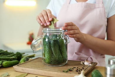 Woman putting bay leaves into pickling jar at table in kitchen, closeup