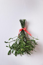 Photo of Mistletoe bunch with red bow hanging on white wooden wall. Traditional Christmas decor