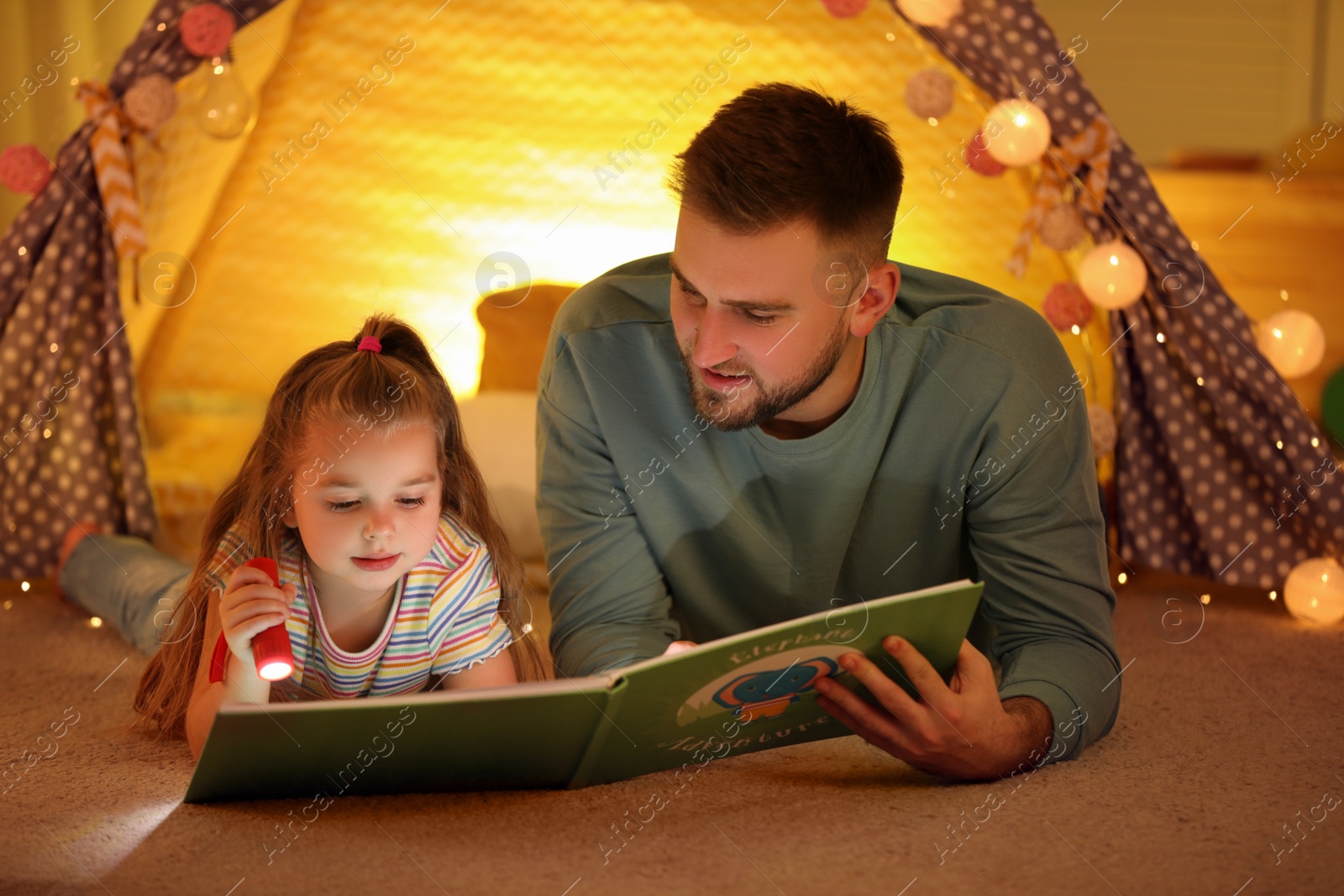 Photo of Father and daughter with flashlight reading book at home