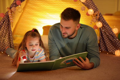 Father and daughter with flashlight reading book at home