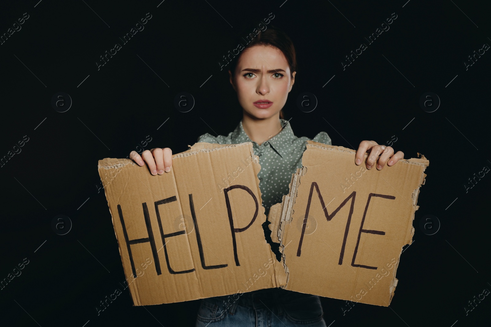 Photo of Unhappy young woman with HELP ME sign on dark background