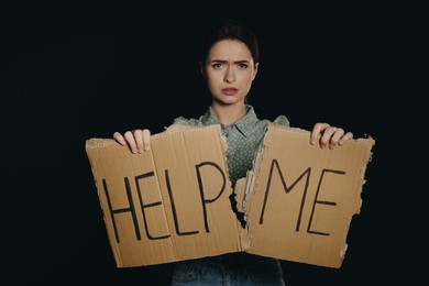 Unhappy young woman with HELP ME sign on dark background