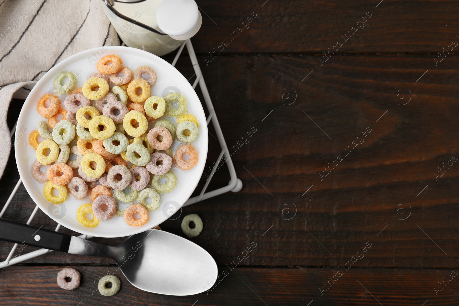 Photo of Cereal rings and milk in bowl on wooden table, top view. Space for text