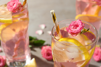 Delicious refreshing drink with rose flowers and lemon slices on light grey table, closeup