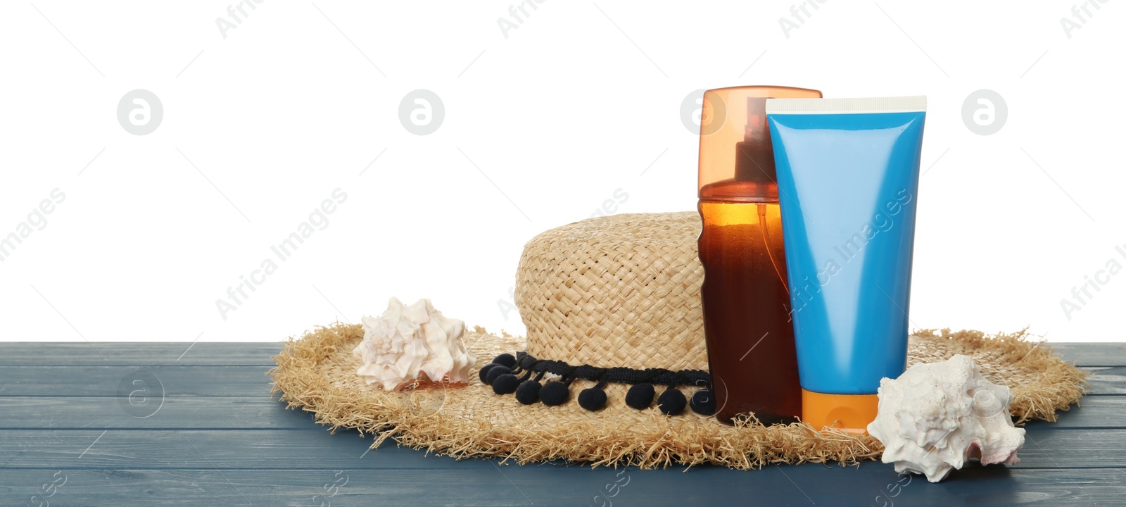 Photo of Sun protection products, shells and beach hat on blue wooden table