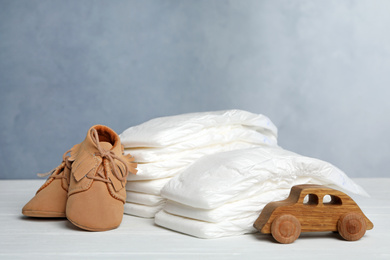Photo of Baby diapers, child's shoes and toy car on white wooden table against grey background