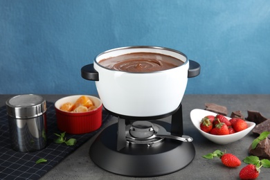 Chocolate fondue in pot and fresh fruits on gray table