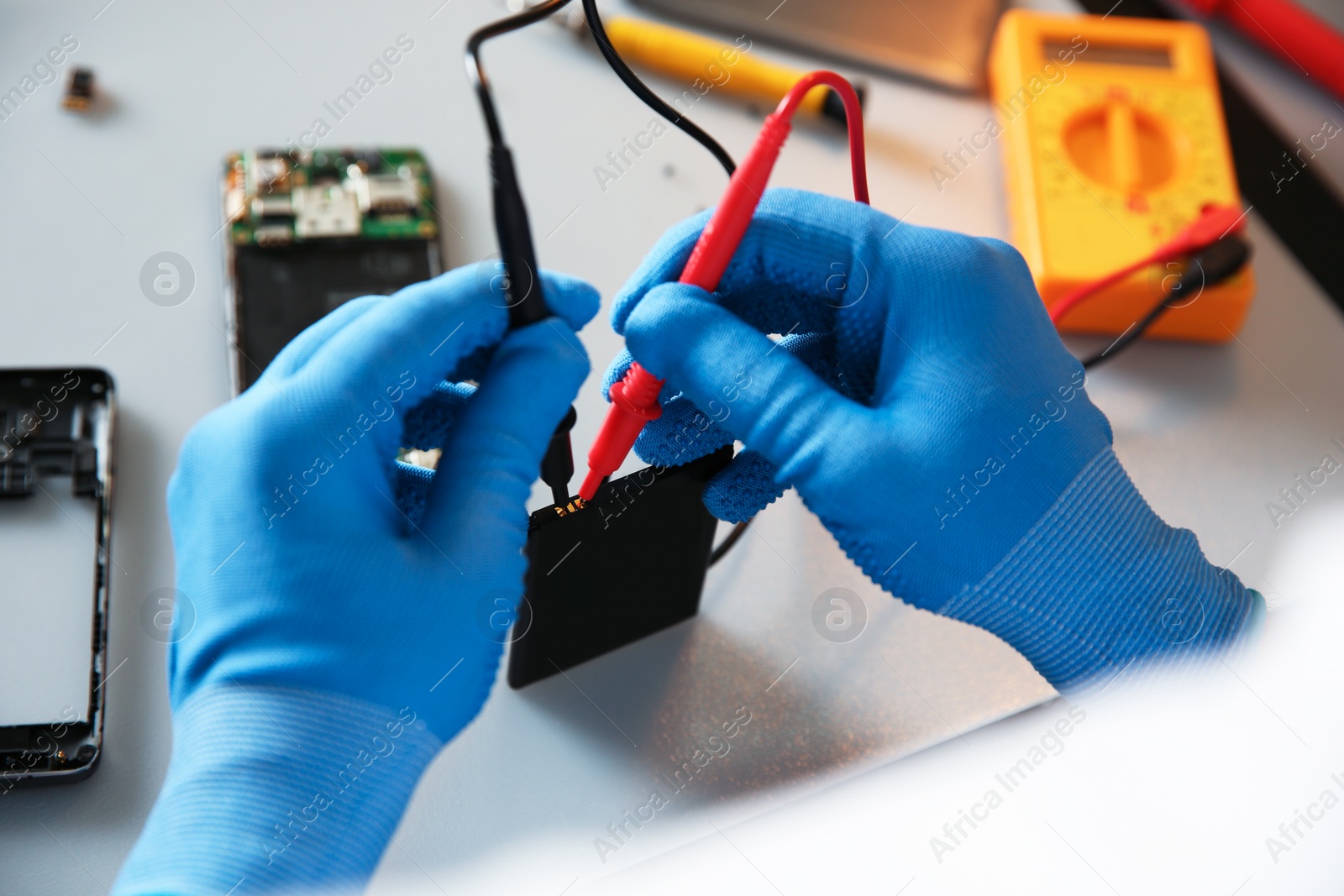 Photo of Technician checking mobile phone battery at table in repair shop, closeup