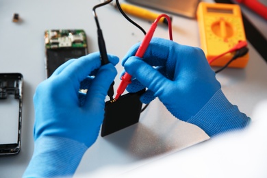 Photo of Technician checking mobile phone battery at table in repair shop, closeup